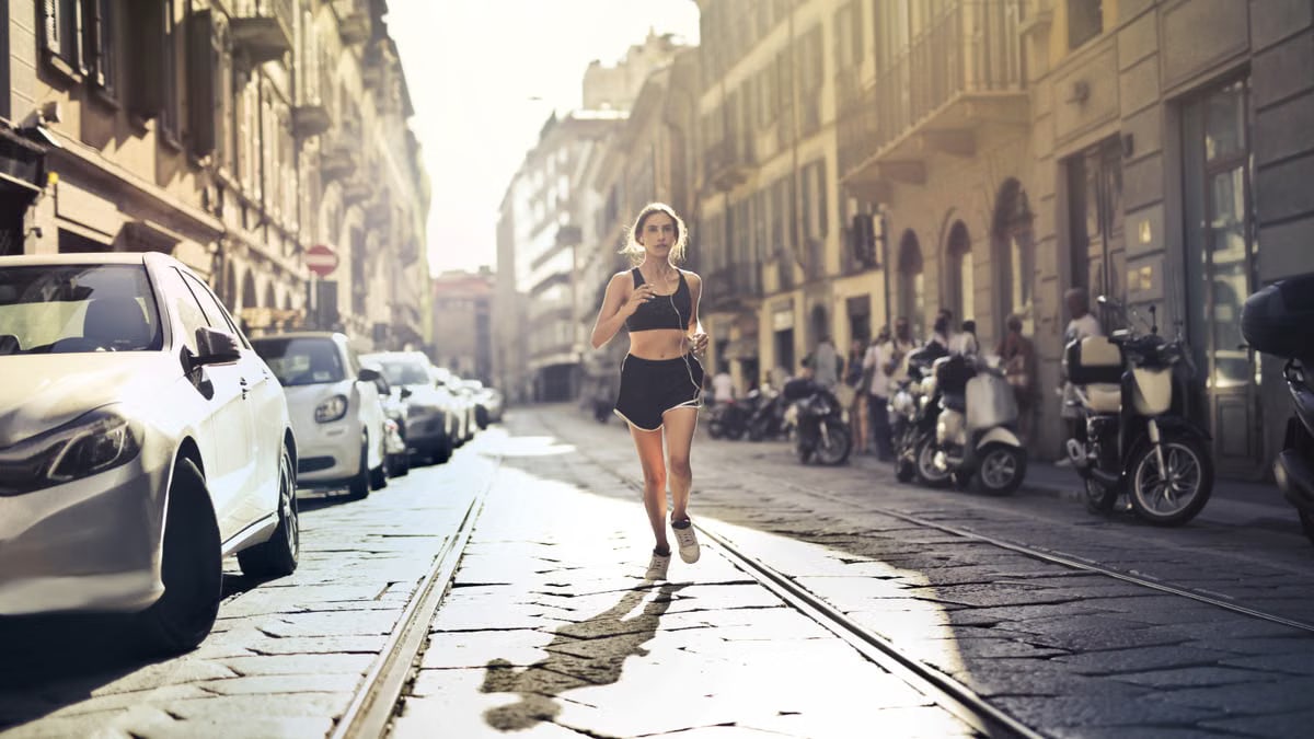 Energetic woman jogger running down a city street in active wear on a sunny day.